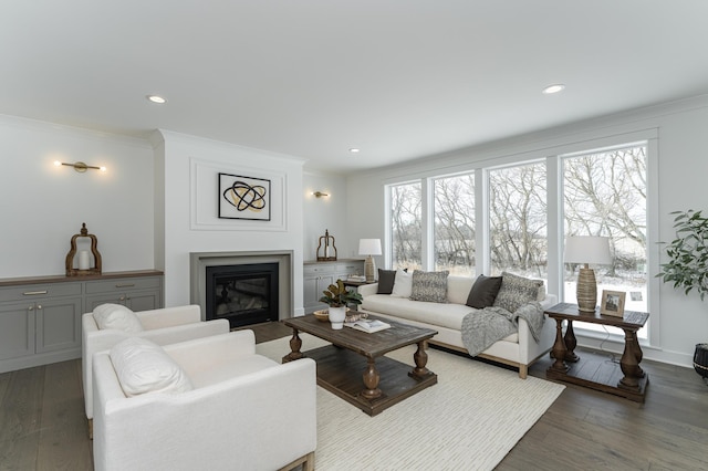 living room with recessed lighting, ornamental molding, dark wood finished floors, and a glass covered fireplace