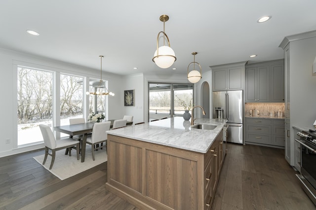 kitchen featuring decorative light fixtures, appliances with stainless steel finishes, a kitchen island with sink, a sink, and light stone countertops