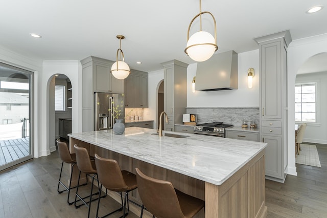 kitchen featuring appliances with stainless steel finishes, arched walkways, a sink, and exhaust hood