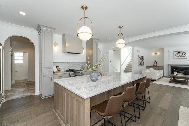 kitchen featuring arched walkways, wall chimney exhaust hood, light stone counters, stainless steel stove, and pendant lighting