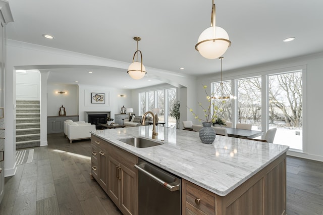 kitchen featuring a kitchen island with sink, a sink, stainless steel dishwasher, light stone countertops, and pendant lighting