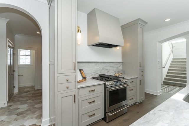 kitchen with light stone counters, arched walkways, stainless steel gas stove, and custom exhaust hood