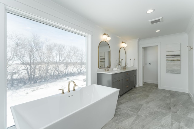 bathroom with double vanity, visible vents, a freestanding bath, ornamental molding, and a sink