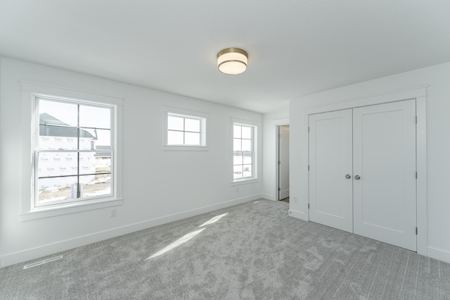 unfurnished bedroom with light carpet, a closet, visible vents, and baseboards