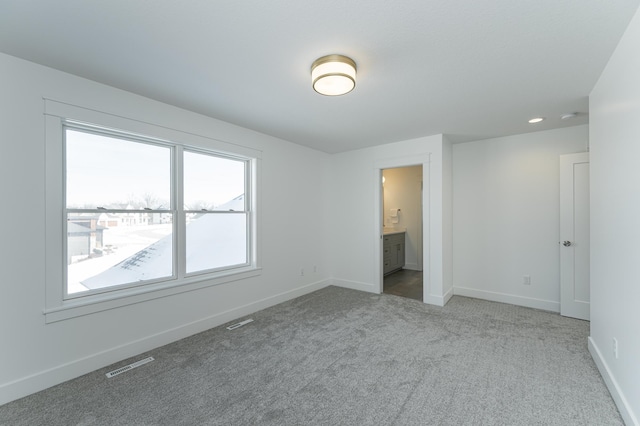 unfurnished bedroom featuring light carpet, baseboards, visible vents, and ensuite bathroom