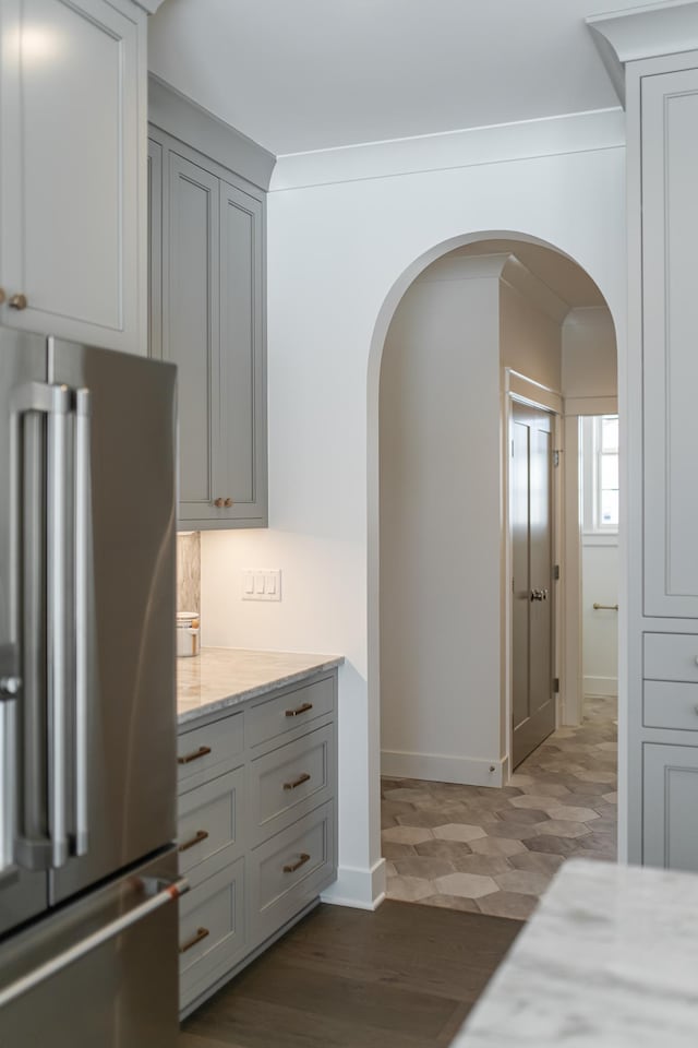 kitchen featuring baseboards, arched walkways, dark wood finished floors, light stone counters, and high end fridge