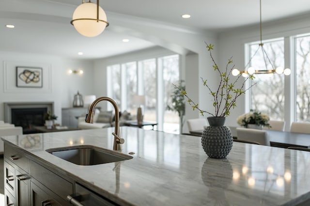 kitchen with light stone counters, pendant lighting, a sink, and open floor plan