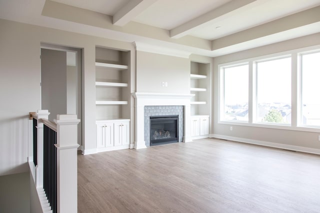 unfurnished living room featuring a fireplace, wood-type flooring, beamed ceiling, and built in shelves