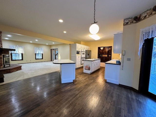 kitchen featuring hanging light fixtures, a kitchen island, dark hardwood / wood-style flooring, a fireplace, and white cabinets