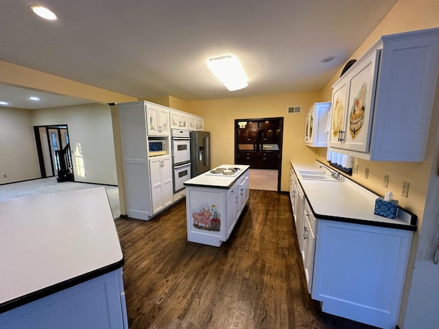 kitchen featuring dark hardwood / wood-style flooring, stainless steel appliances, sink, white cabinets, and a center island