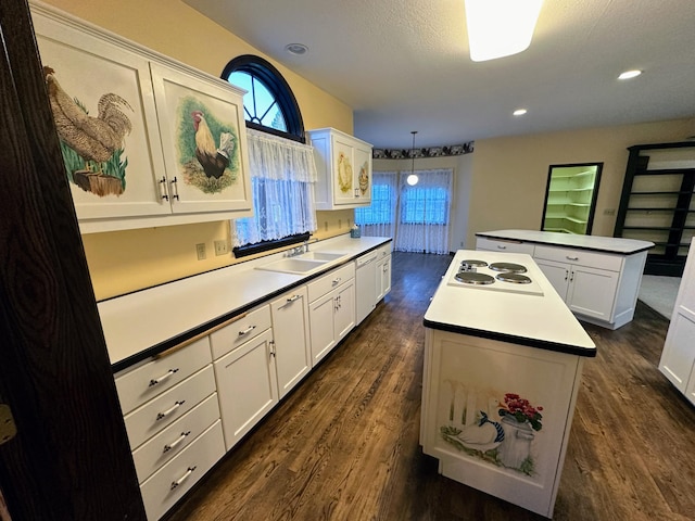 kitchen with dark wood-type flooring, white cabinets, sink, decorative light fixtures, and a kitchen island