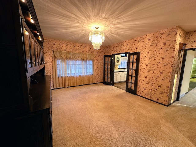 empty room featuring french doors, carpet floors, and an inviting chandelier