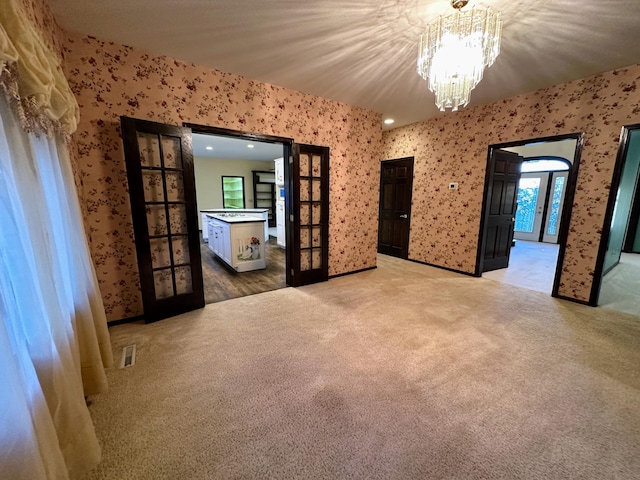 spare room featuring french doors, carpet floors, and a notable chandelier