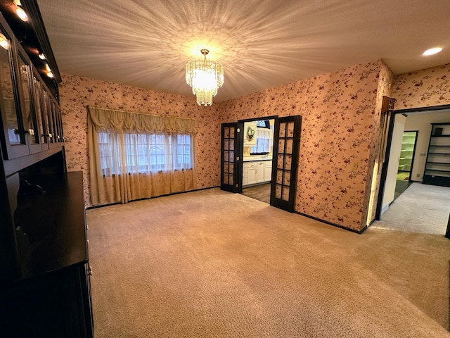 carpeted empty room with french doors and a chandelier