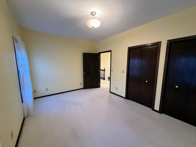 unfurnished bedroom with a textured ceiling, light colored carpet, and multiple closets