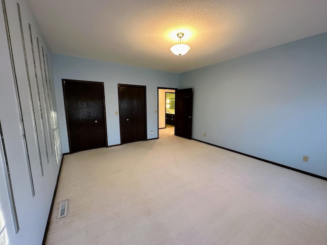 unfurnished bedroom with two closets, a textured ceiling, and light colored carpet