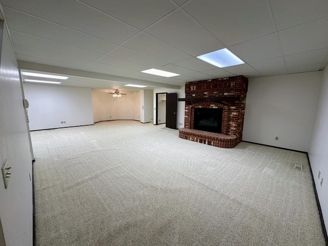 unfurnished living room with a drop ceiling, light colored carpet, and a brick fireplace