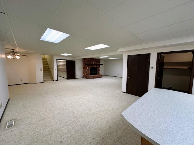 basement with a drop ceiling, ceiling fan, light colored carpet, and a fireplace