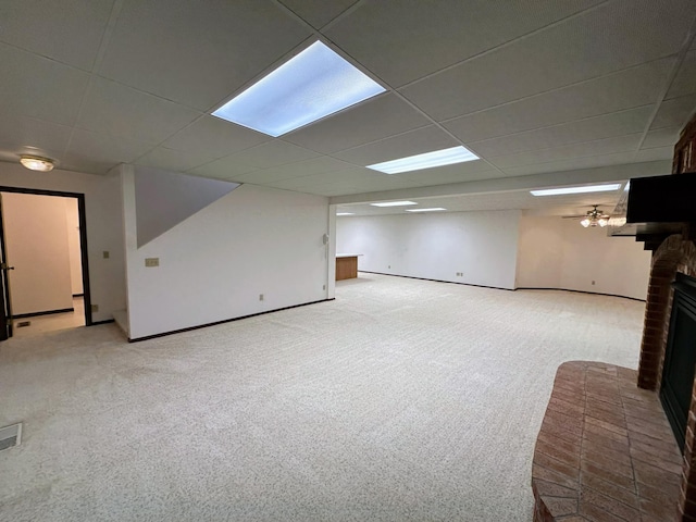 basement with a paneled ceiling, light colored carpet, and a brick fireplace