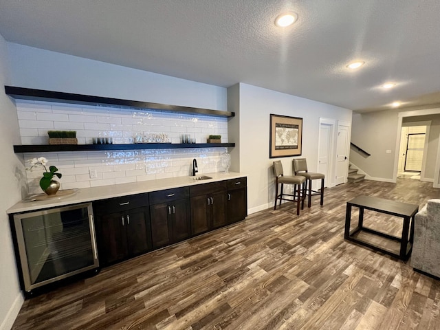 bar featuring beverage cooler, dark wood-type flooring, backsplash, a textured ceiling, and dark brown cabinetry