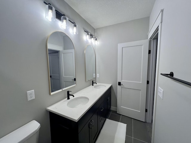 bathroom featuring tile flooring, a textured ceiling, double vanity, and toilet