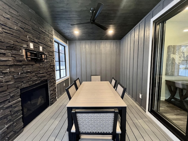 dining area featuring wood walls, ceiling fan, light wood-type flooring, and a fireplace