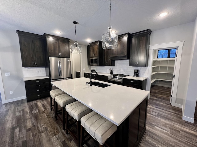 kitchen featuring dark wood-type flooring, stainless steel appliances, backsplash, decorative light fixtures, and sink