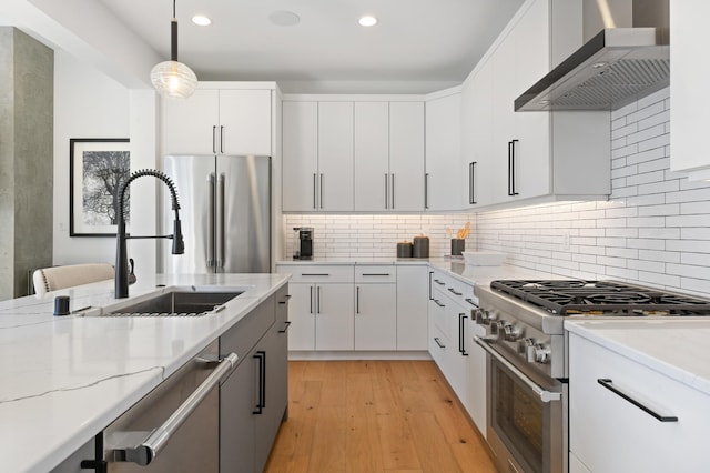 kitchen with white cabinetry, premium appliances, decorative light fixtures, and wall chimney range hood