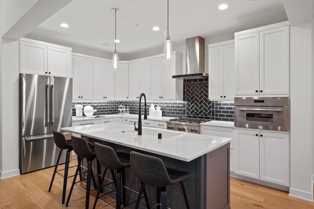 kitchen with white cabinets, appliances with stainless steel finishes, a center island with sink, and wall chimney range hood