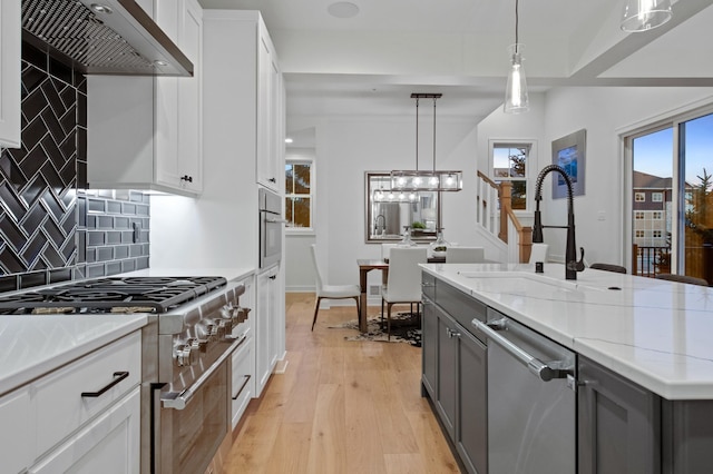 kitchen with decorative light fixtures, white cabinetry, stainless steel appliances, light stone countertops, and wall chimney range hood