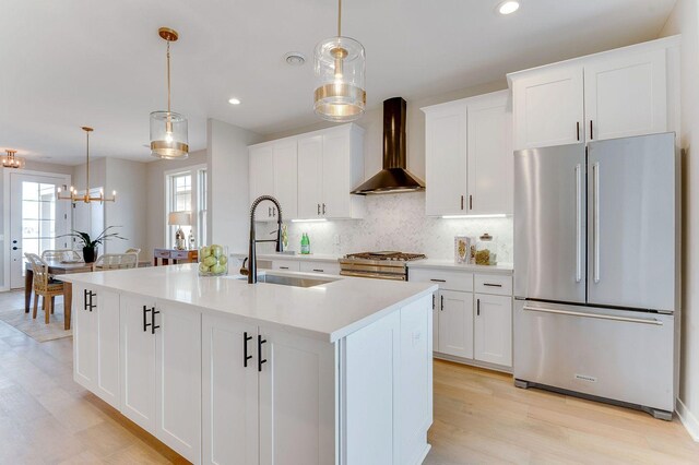 kitchen with wall chimney exhaust hood, decorative light fixtures, a center island with sink, white cabinets, and appliances with stainless steel finishes