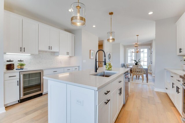 kitchen with decorative light fixtures, a center island with sink, beverage cooler, and sink