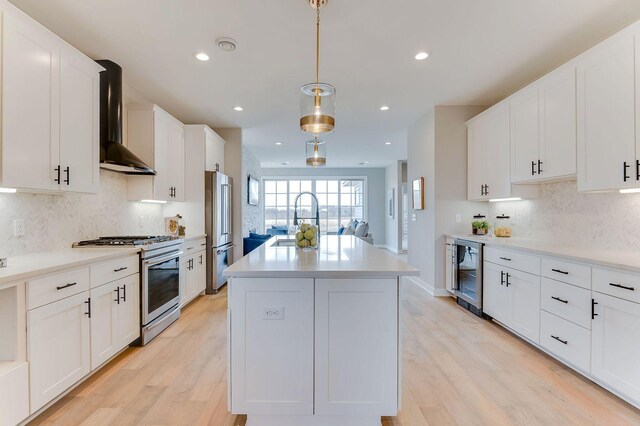 kitchen with appliances with stainless steel finishes, wall chimney exhaust hood, beverage cooler, sink, and hanging light fixtures