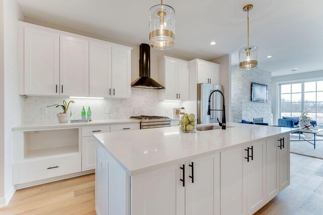 kitchen featuring pendant lighting, wall chimney range hood, sink, and a kitchen island with sink