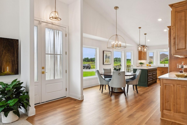 dining room with vaulted ceiling, an inviting chandelier, sink, and light hardwood / wood-style flooring