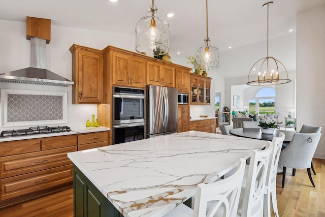 kitchen with hanging light fixtures, wall chimney exhaust hood, stainless steel appliances, and lofted ceiling