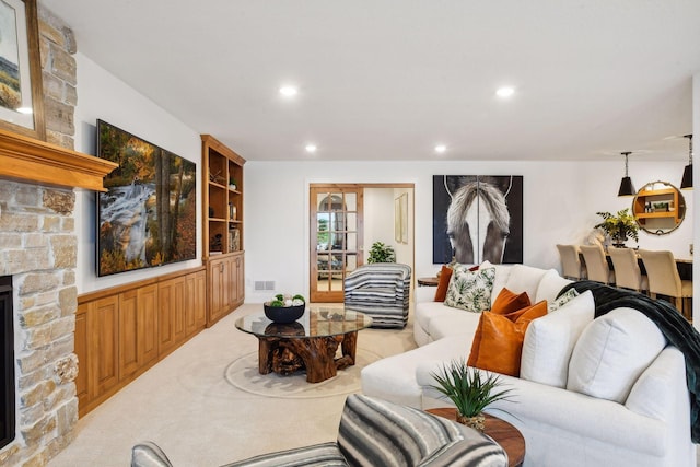 living room featuring built in shelves, a stone fireplace, and light colored carpet