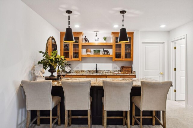 kitchen featuring sink, decorative light fixtures, light stone counters, and a breakfast bar area