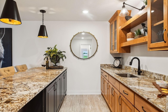 kitchen with light hardwood / wood-style flooring, light stone counters, hanging light fixtures, and sink