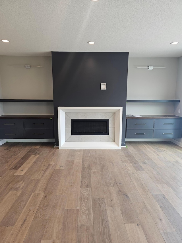 unfurnished living room featuring a tiled fireplace, recessed lighting, wood finished floors, and a textured ceiling