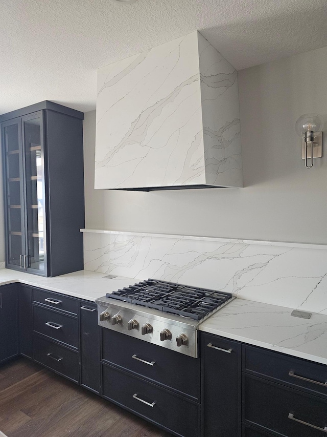 kitchen featuring glass insert cabinets, stainless steel gas cooktop, dark cabinets, a textured ceiling, and dark wood-style flooring