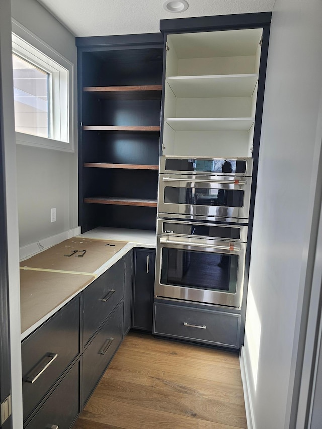 kitchen with stainless steel double oven, light wood-style flooring, light countertops, and open shelves