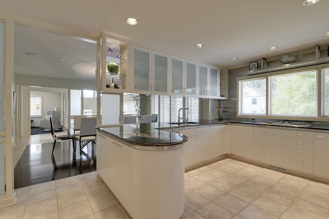 kitchen featuring kitchen peninsula, sink, dark stone counters, and white cabinets