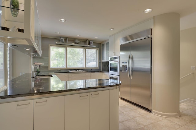 kitchen with sink, white cabinets, tasteful backsplash, dark stone countertops, and built in fridge