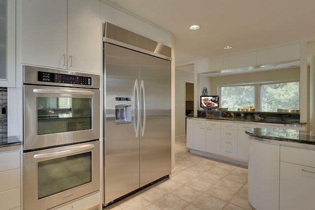 kitchen featuring white cabinetry, decorative backsplash, dark stone counters, and appliances with stainless steel finishes