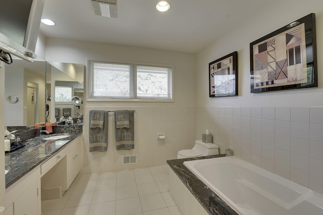 bathroom with a relaxing tiled tub, tile patterned floors, vanity, and toilet