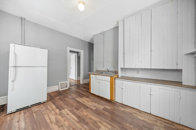 kitchen with white cabinetry, a textured ceiling, wood-type flooring, white refrigerator, and sink