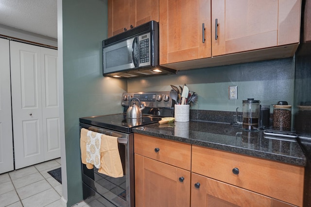 kitchen featuring stainless steel range with electric stovetop, dark stone countertops, light tile patterned floors, and a textured ceiling