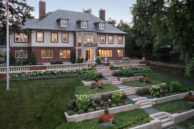 back of house at dusk featuring a yard, brick siding, and a chimney