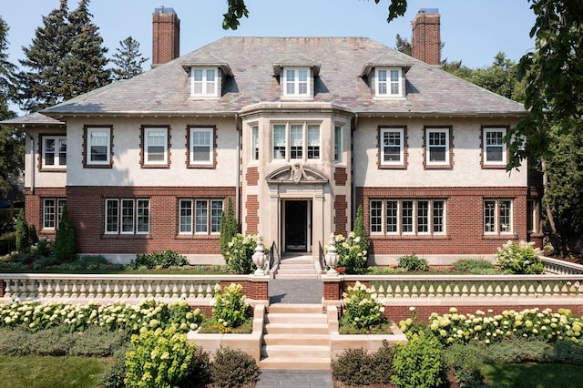 georgian-style home featuring a high end roof, stucco siding, brick siding, and a chimney